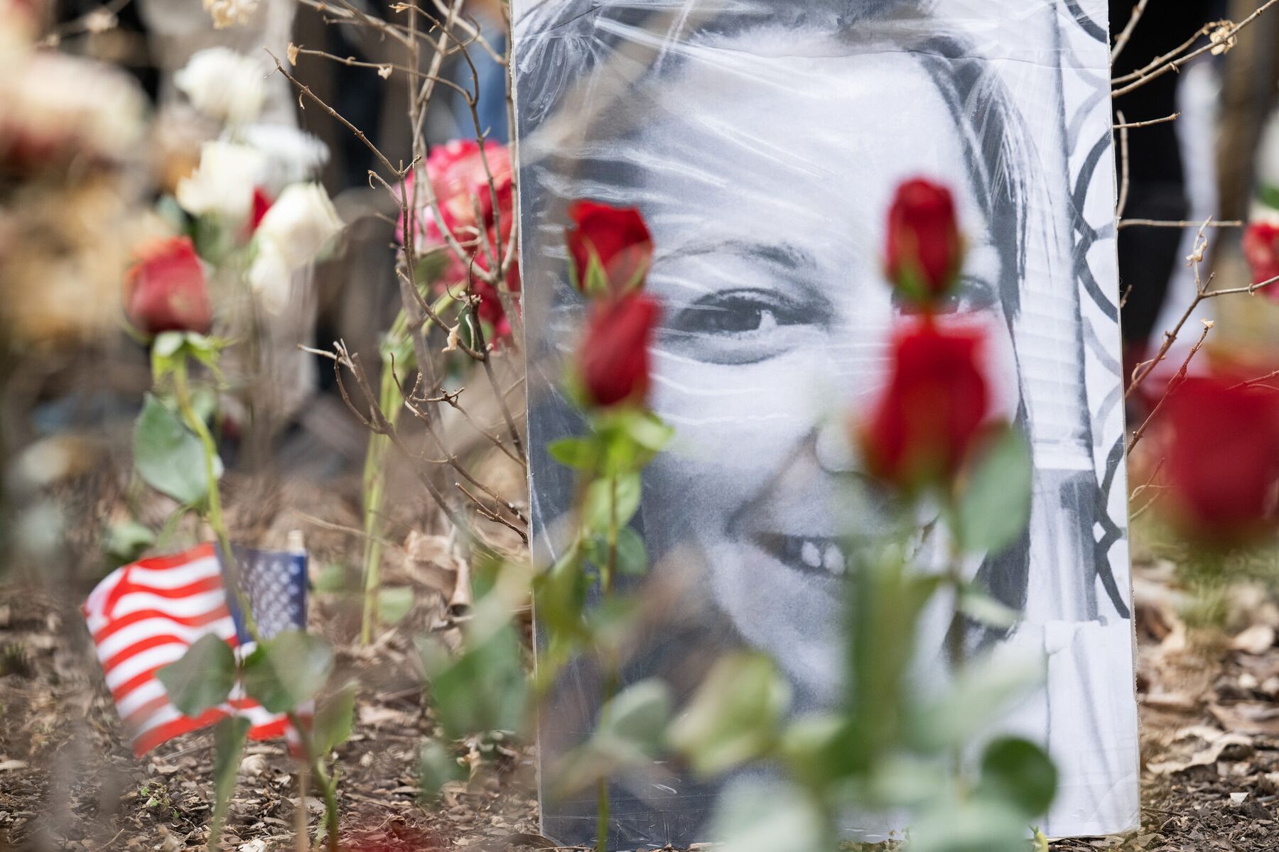 Red roses and a small American flag placed around a black-and-white portrait at a memorial