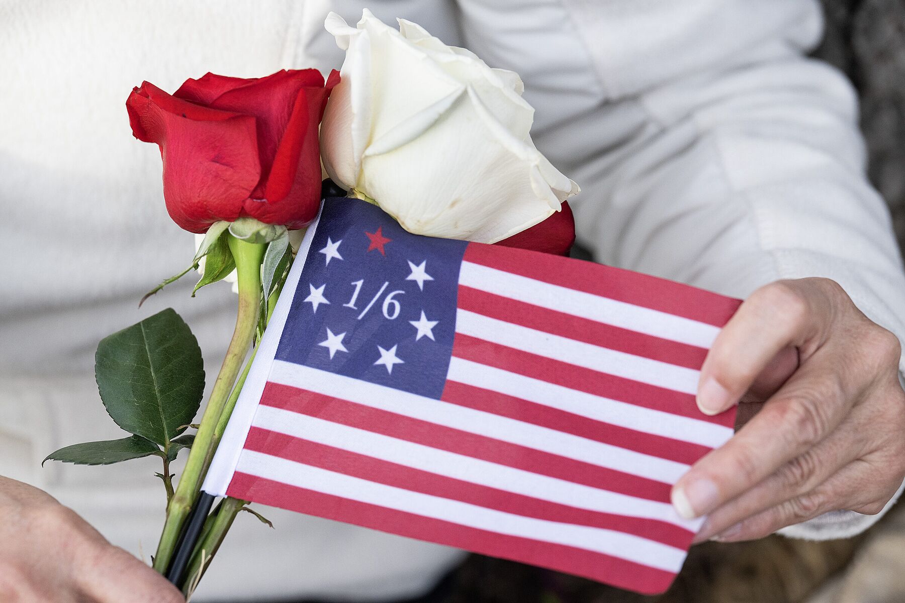 Hands holding a red rose, a white rose, and a small American flag marked 1/6