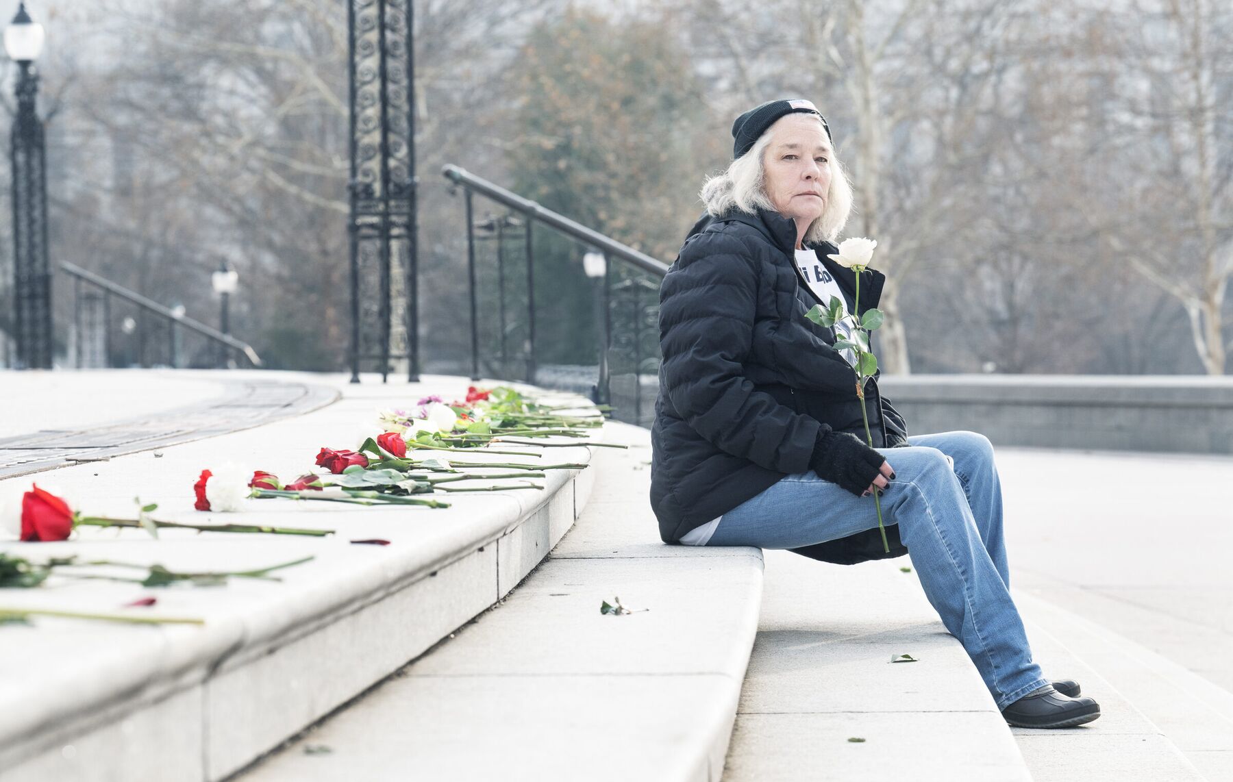 A woman sits alone on the Capitol steps holding a white rose beside a line of red and white roses
