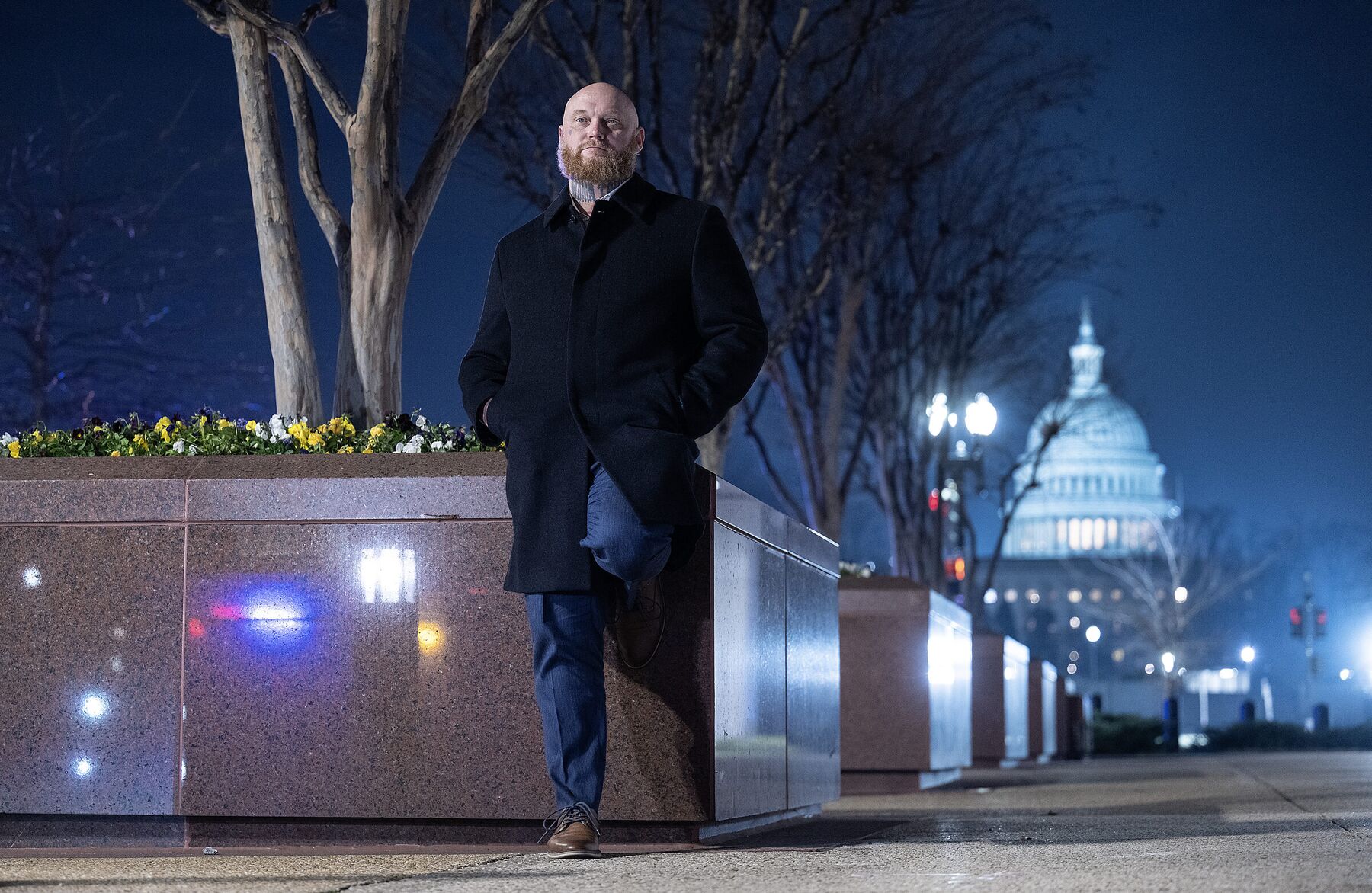 A man standing on a Washington, D.C. sidewalk at night with the U.S. Capitol in the distance